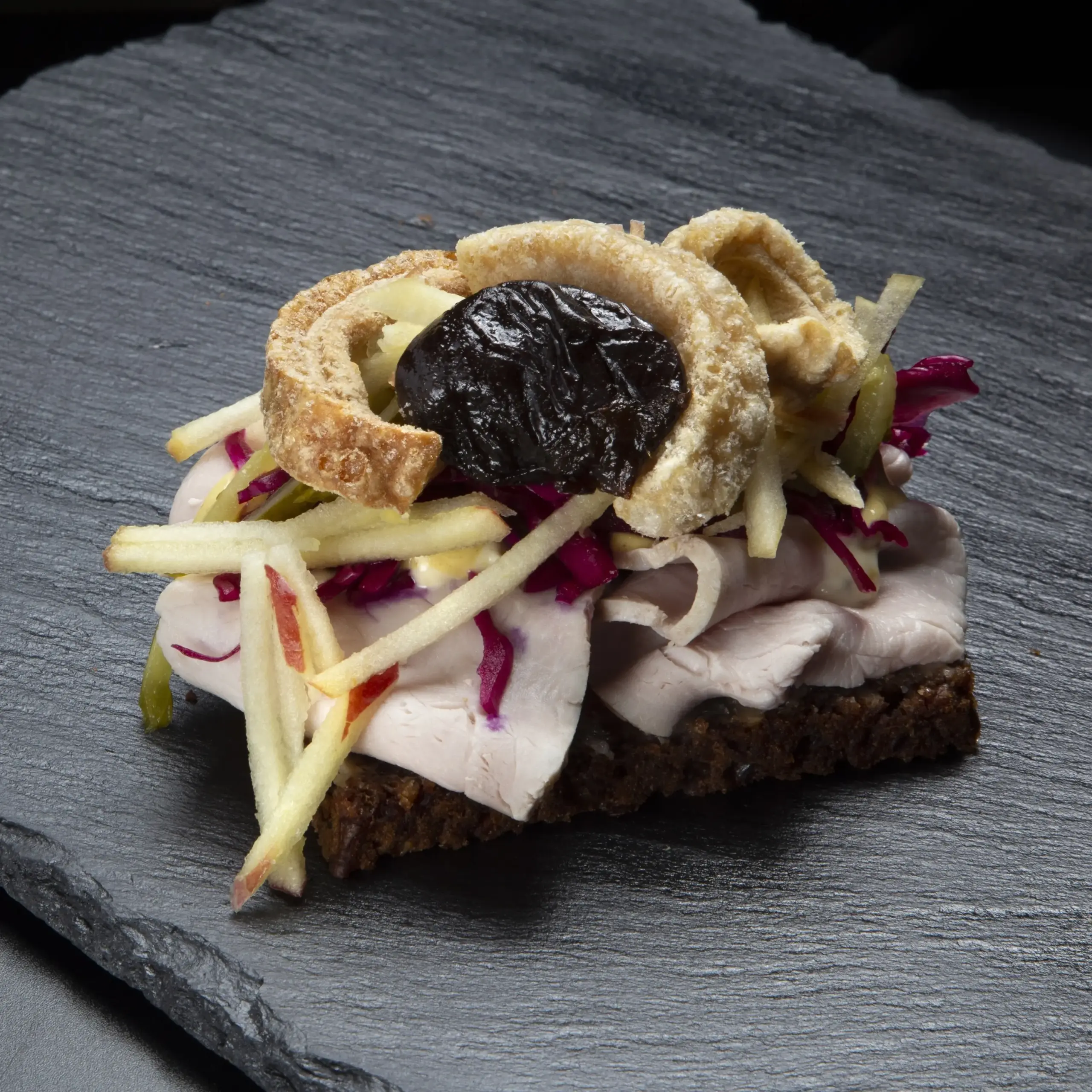 Smørrebrød med økologisk flæskesteg på rugbrød fra Ibens Smørrebrød i København med sprøde svær, rødkål, syltet agurk, æble og svesker
