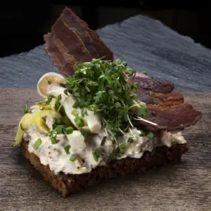Smørrebrød med hjemmelavet hønsesalat på rugbrød fra Ibens Smørrebrød i København med sprød bacon, syltede agurker, syltet rødløg og karse
