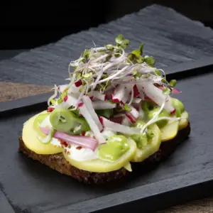 Smørrebrød kartoffelmad på rugbrød fra Ibens Smørrebrød i København med nye danske kartofler, rygeostcreme, syltet rødløg, radiser og urtemayo