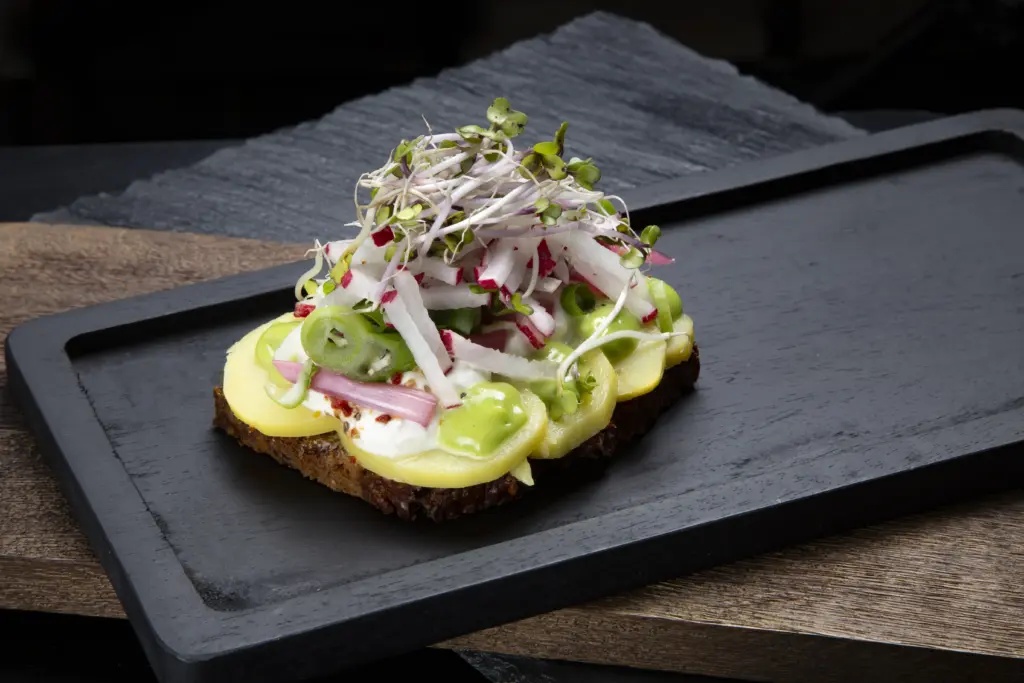 Smørrebrød kartoffelmad på rugbrød fra Ibens Smørrebrød i København med nye danske kartofler, rygeostcreme, syltet rødløg, radiser og urtemayo