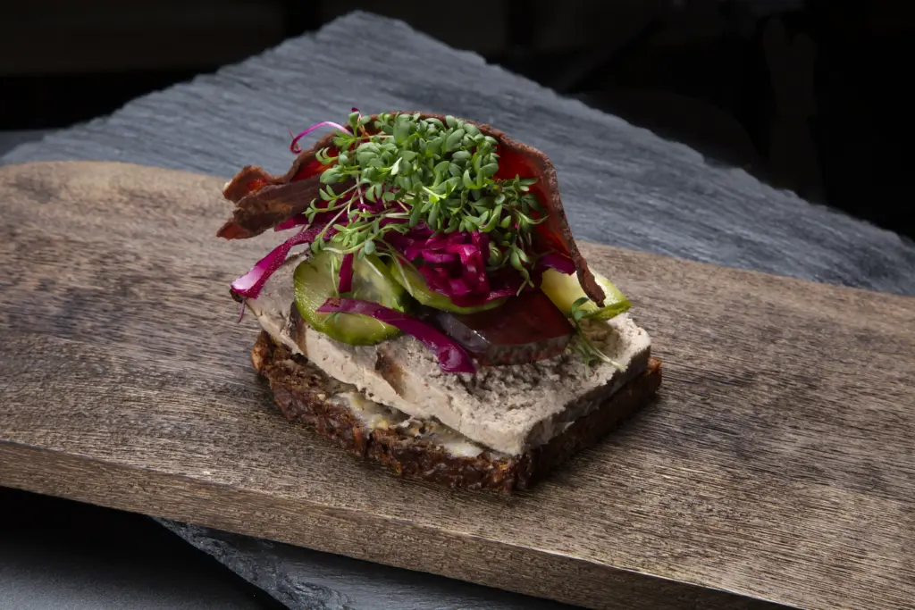 Smørrebrød med leverpostej på rugbrød fra Ibens Smørrebrød i København med hjemmesyltede agurker, rødkål, sprød bacon og karse