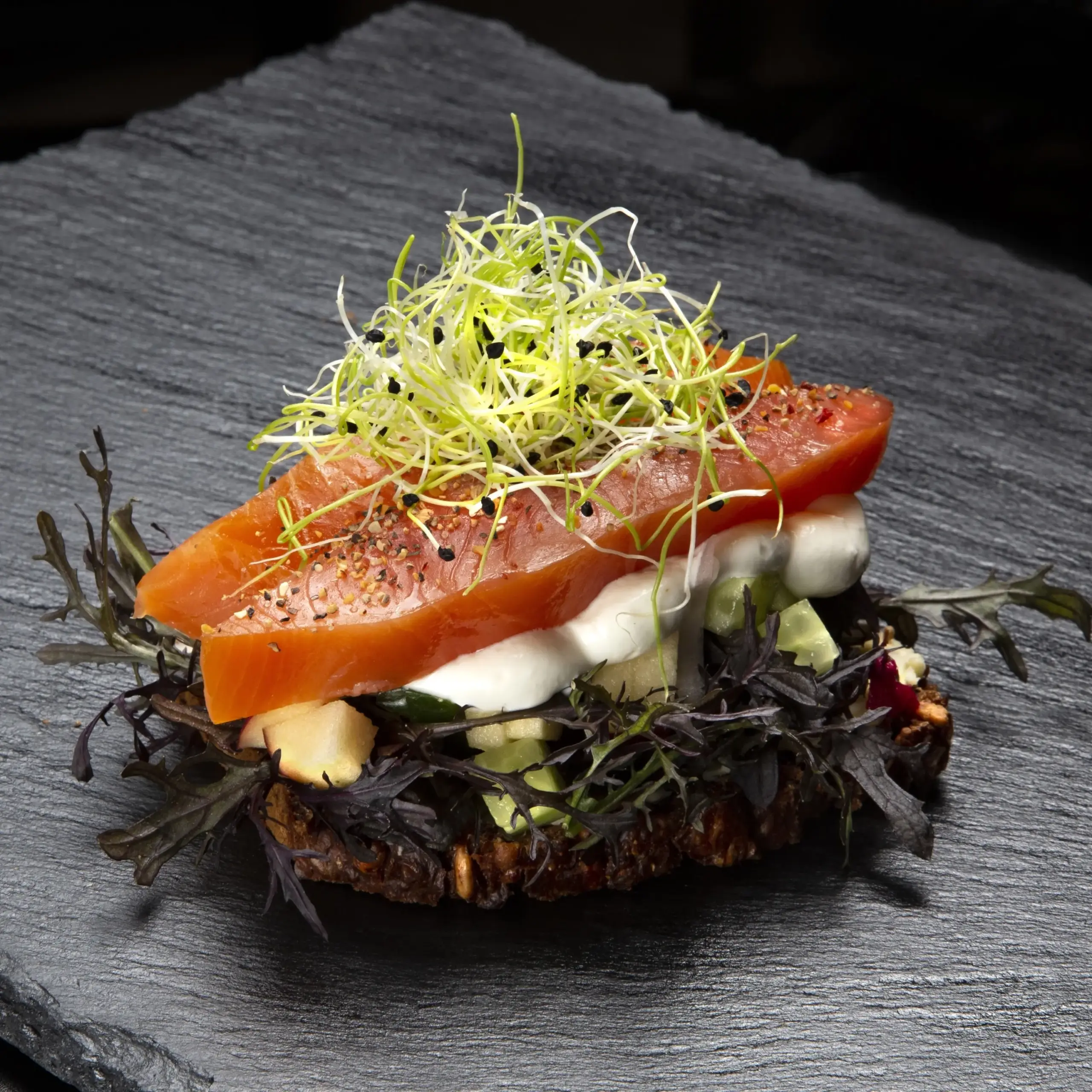 Smørrebrød med røget laks på rugbrød fra Ibens Smørrebrød i København med æble, agurk, rødløg, rygeostcreme, grov peber og spirer
