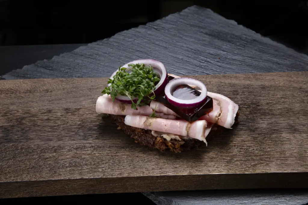 Smørrebrød med rullepølse på rugbrød fra Ibens Smørrebrød i København slagterens traditionelle danske rullepølse med sky, rødløg og karse