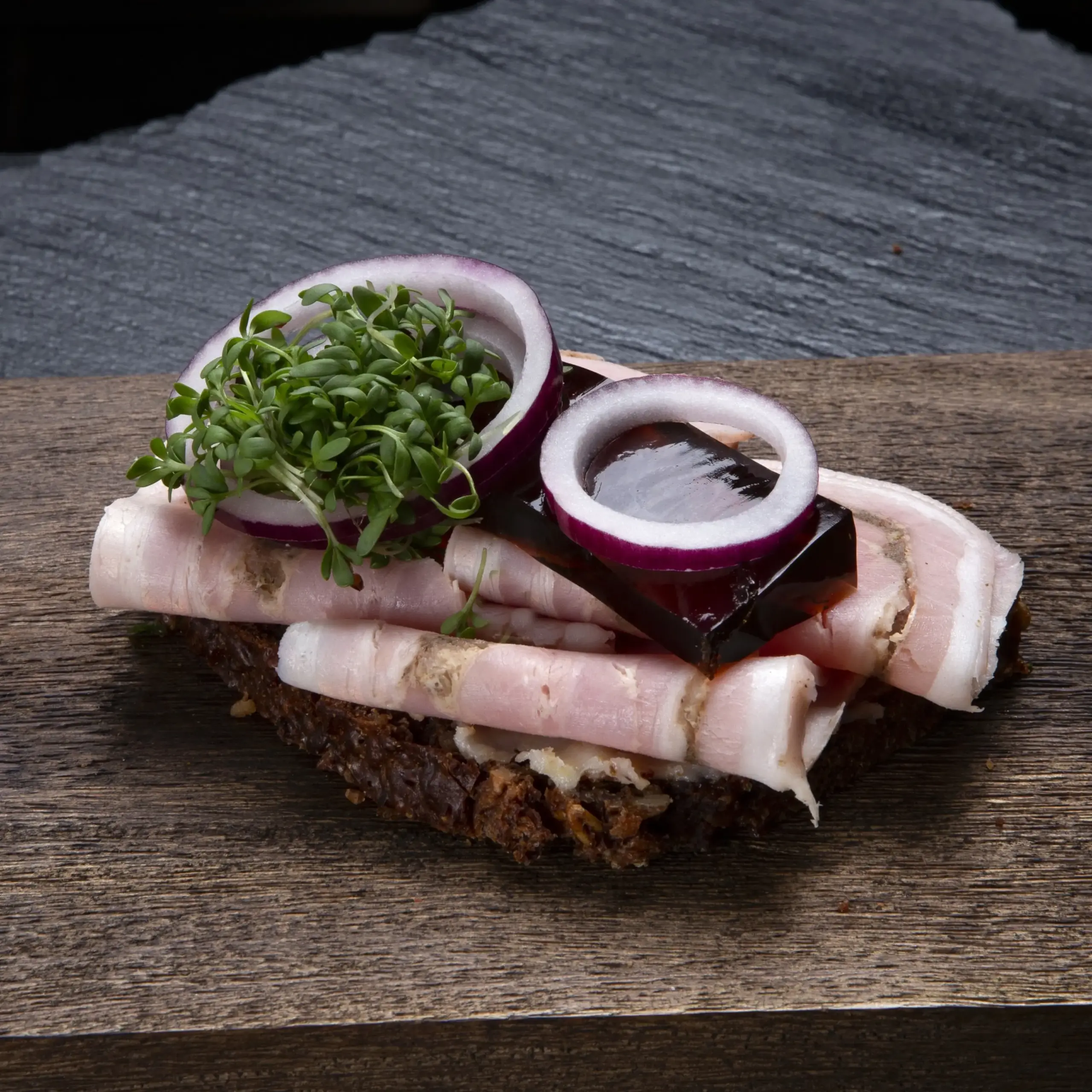 Smørrebrød med rullepølse på rugbrød fra Ibens Smørrebrød i København slagterens traditionelle danske rullepølse med sky, rødløg og karse