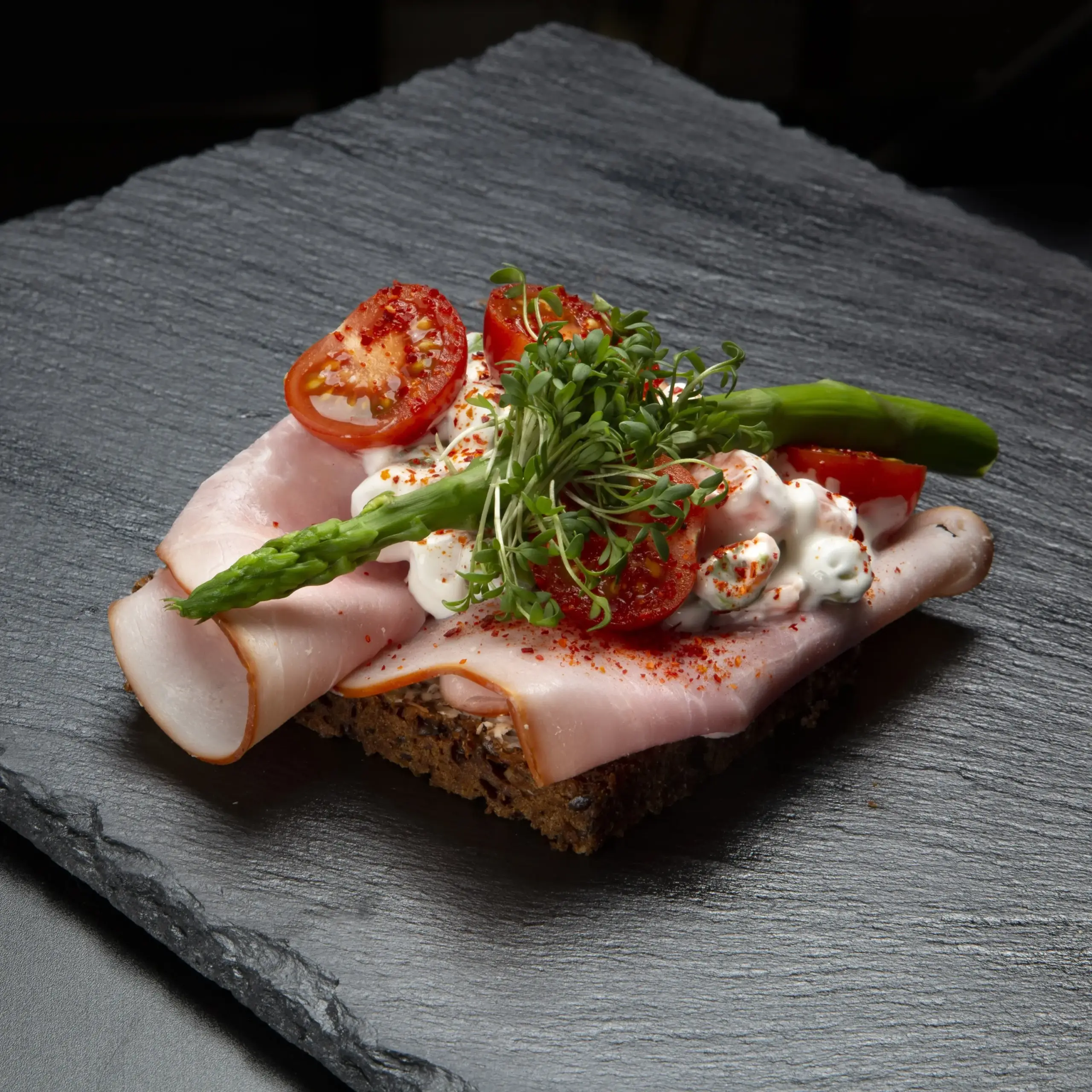 Smørrebrød med røget dansk skinke på rugbrød fra Ibens Smørrebrød i København med italiensk salat, sprøde asparges, tomat, piment d’Espelette og karse