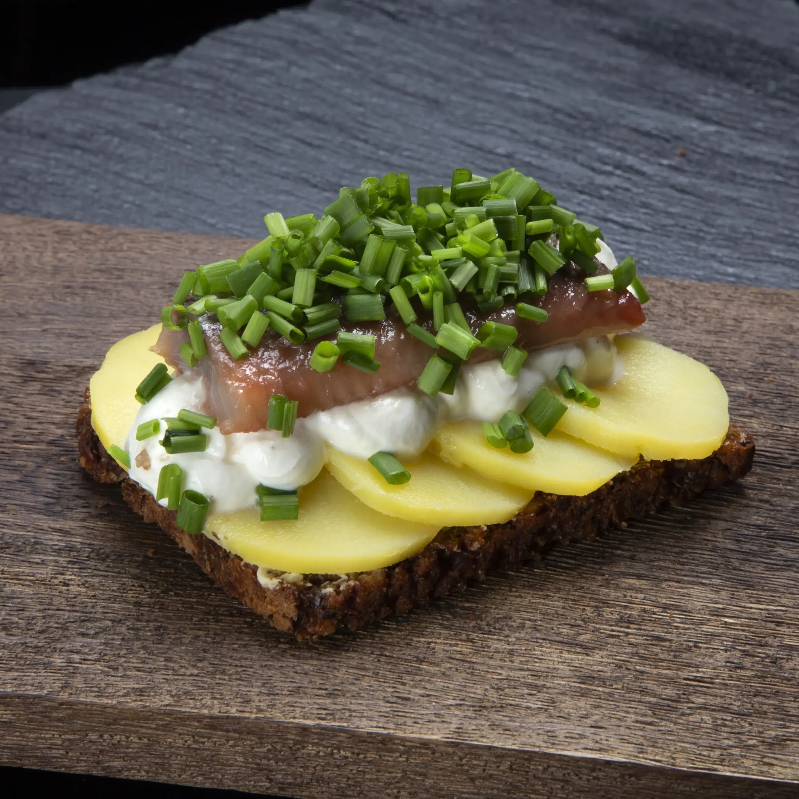Smørrebrød med nye danske kartofler og svensk matjessild på rugbrød fra Ibens Smørrebrød i København med rygeostcreme, purløg og friske krydderurter