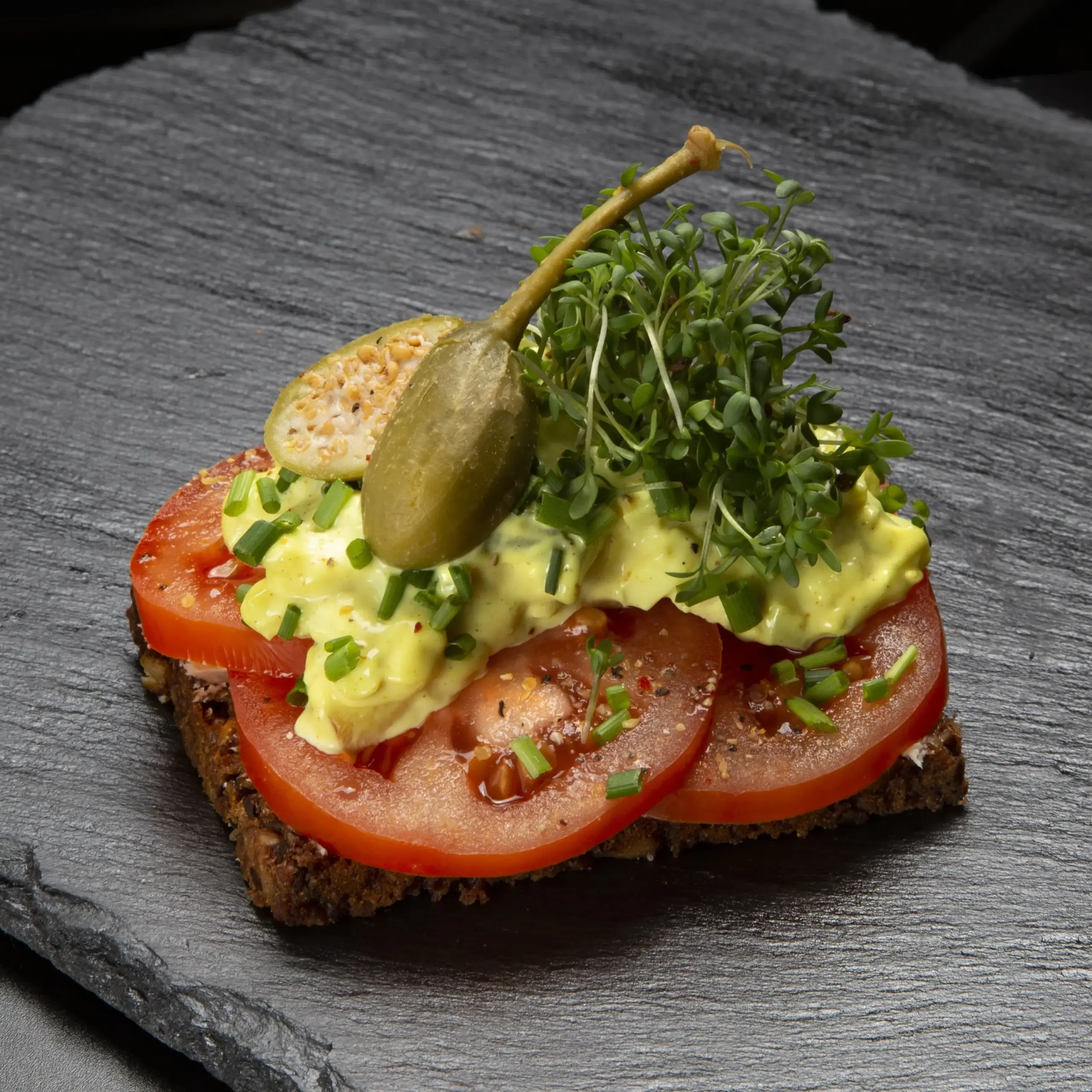 Vegetarisk smørrebrød med solmodne danske tomater på rugbrød fra Ibens Smørrebrød i København med æggesalat, friske krydderurter, kapersbær og karse